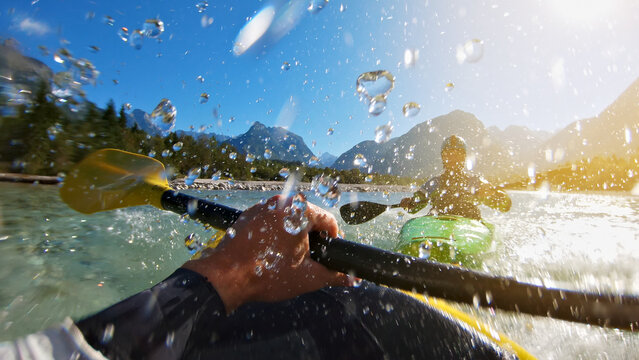 A thrilling kayaking adventure unfolds as two kayakers paddle through a scenic river surrounded by majestic mountains. A close-up shot captures the splashes of water.