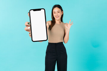Cheerful beautiful Asian women holding smart phone mockup of blank screen and shows ok sign on blue background.