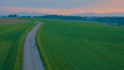 An aerial view captures three cyclists riding on a winding road through a vast green field, showcasing their endurance and passion for road cycling. The scene highlights the beauty of nature and the.