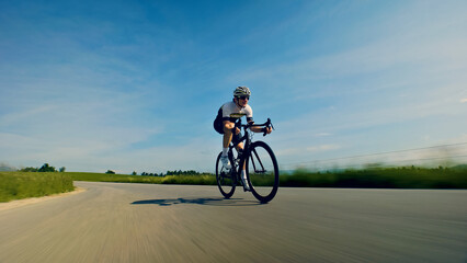 Obraz premium A thrilling close-up shot of a helmeted cyclist skillfully navigating a winding road, surrounded by lush greenery and a clear blue sky. The dynamic perspective emphasizes the speed and intensity of.