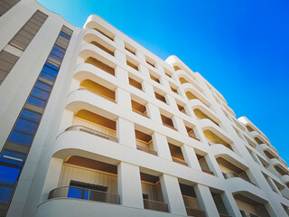 Fragment of a beautiful modern white facade of a multi-story hotel or house with large loggias against the background of a blue sky. Close-up.
