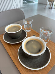 Two cups of hot americano coffee and water on wooden tray