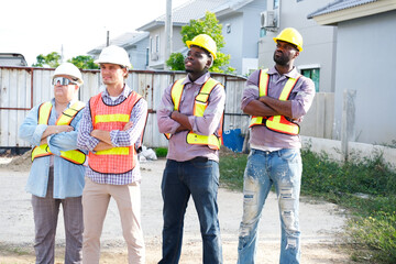 A team of male engineers wearing safety helmets is smiling while standing at the construction site.