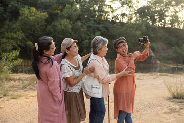Four Asian senior women standing in line smiling laughing posing for camera held by front friend during outdoor travel trip enjoying fun moment friendship nature adventure under warm sunlight