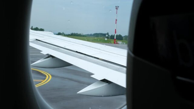 A view from the porthole to the wing of driving passenger airplane along the runway. Aviation. Air transportation. The overcast weather. High quality 4k footage.