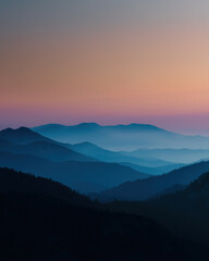Obraz premium Misty mountain range at sunset with layered blue hills and soft gradient sky creating peaceful and serene atmosphere in nature