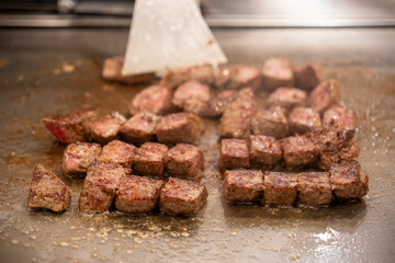 Diced beef cubes searing on commercial kitchen griddle with spatula for restaurant cooking preparation