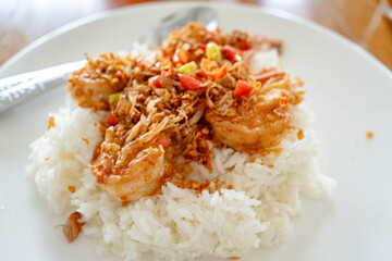 Stir Fried Shrimp and cooked rice topped  in white plate on wooden table at restaurant.Top view