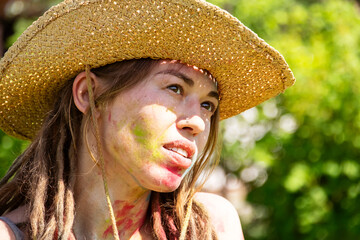 Woman with Colorful Holi Powder Splashes on Her Face Wearing Straw Hat. Festival Celebrating Indian Culture.