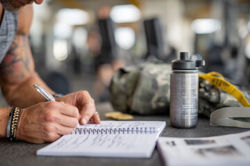 Athlete marking progress in a workout journal, writing down weights and reps, gym bag and water bottle in background, motivational and determination.