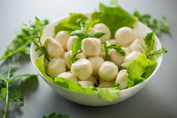 Mini mozzarella balls with herbs in white bowl on grey background