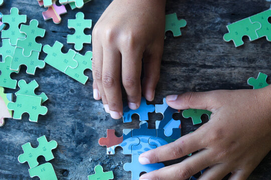 hands playing jigsaw puzzle on wooden table - Powered by Adobe