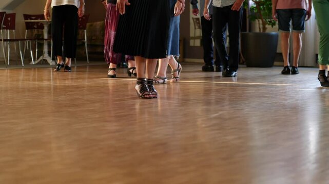 Low angle of the feet of dancers while they are training in a dancing class, the floor is parquet