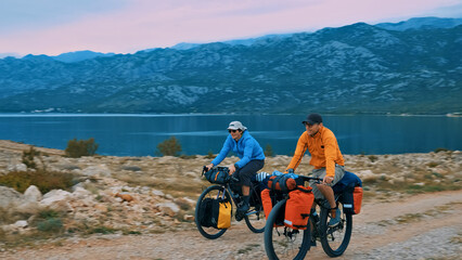 Two cyclists ride their loaded bikes along a scenic mountain road, enjoying the breathtaking view...