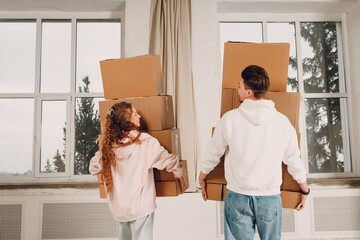 Happy young family couple man and woman moving with cardboard boxes to new estate home apartment. Rear back view.