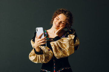 Portrait of a young aristocratic woman holding mobile phone dressed in a medieval dress on dark background