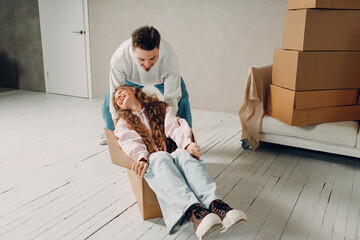 Happy young family couple man push woman inside box. Moving with cardboard boxes to new estate home apartment concept