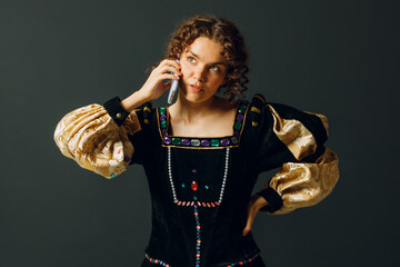 Portrait of a young aristocratic woman talking on mobile phone dressed in a medieval dress on dark background