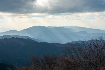 冬の金剛山ちはや園地展望台から見た、雲間から差し込む光芒が照らす広がる山々の風景
