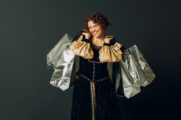 Portrait of a young adult woman dressed in a medieval dress holding shopping bags in hands