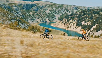 A thrilling aerial view showcases two cyclists, one in a blue jacket and the other in an orange...