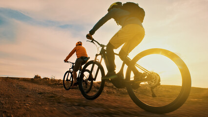 Obraz premium Two helmeted cyclists ride off-road bikes on a dirt trail at sunset. A close-up shot highlights their speed and freedom, showcasing the exhilaration of off-road biking.