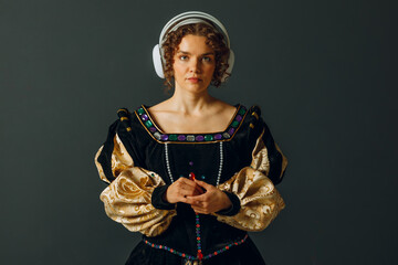 Portrait of a young aristocratic woman with headphones on her head and dressed in a medieval dress listens classical music