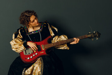 Portrait of a young adult woman playing classical music on electric guitar and dressed in a medieval dress