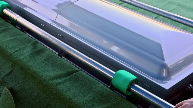 Silver coffin casket is placed above freshly dug grave with green grass, silent surroundings during burial ceremony.