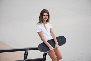 Young attractive girl in a white t-shirt and denim shorts holding skateboard.