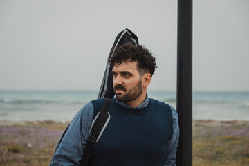 Guitarist Waits for Someone Leaning Against a Pole Near the Sea