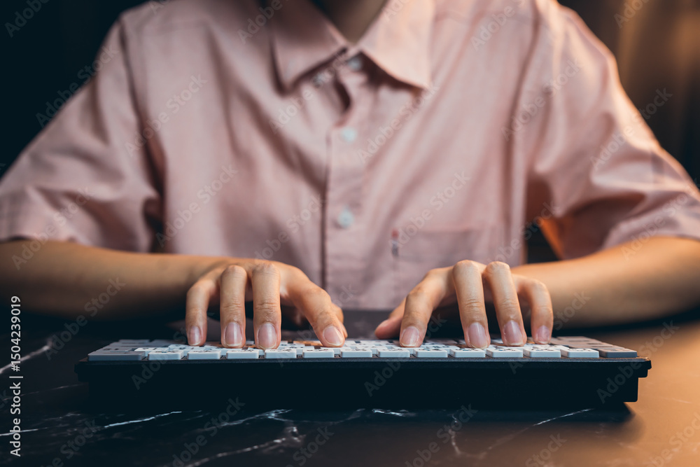 Poster young person typing on a keyboard in a low-light setting with focused expression on a dark marble su