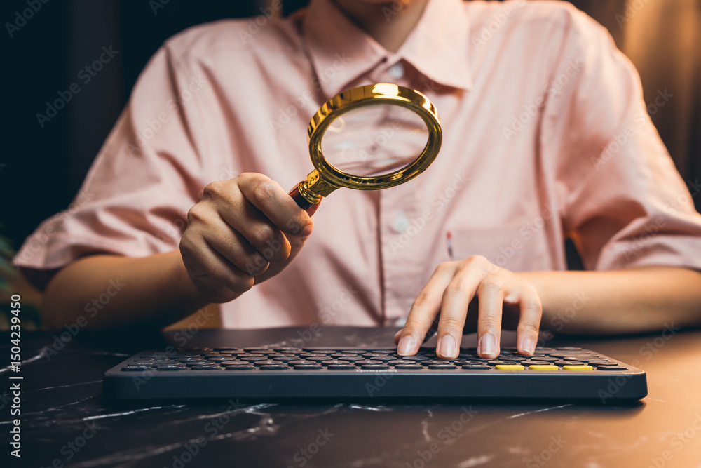 Poster person holding magnifying glass while typing on keyboard in a modern workspace setting