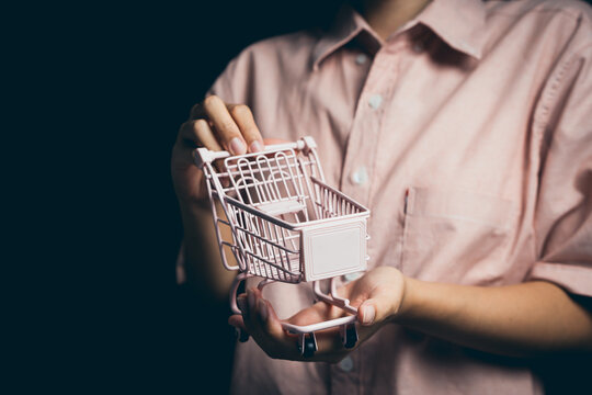 Miniature Shopping Cart in Hand on Dark Background, Symbolizing Retail, E-commerce, and Consumer Behavior Concepts