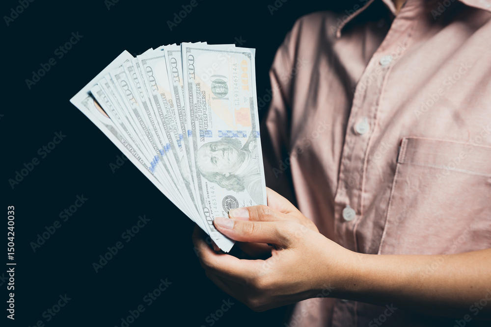 Poster hand holding stack of dollar bills with focused attention on currency in a dark background