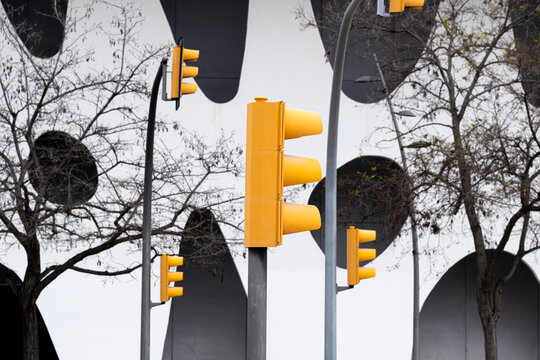 Yellow traffic lights in front of an artistic facade with circular cutouts and tree branches, offering pattern, color and design for modern urban visuals.
