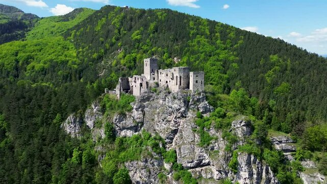 Drone footage reveals the majestic ruins of Strečno Castle perched dramatically on a limestone cliff above the V&aacute;h River, surrounded by the lush, mountainous forests of northern Slovakia