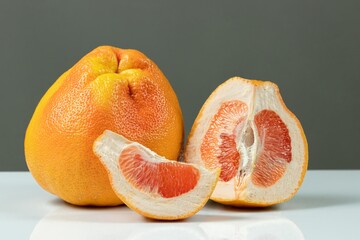 Whole and cut grapefruits on gray background. Texture of juicy citrus pulp and dimple peel.