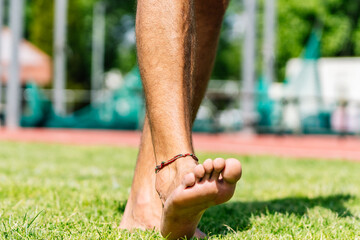 Athlete walking barefoot on grass at a running track: focus on feet