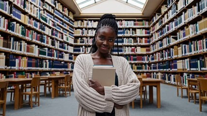 Young woman smiling while holding books in a library setting, university library study