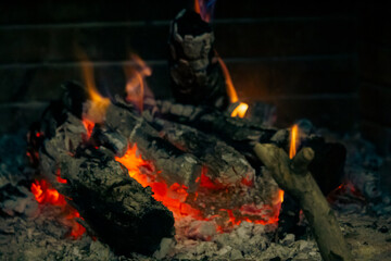 Close-up of glowing embers and charred wood in a fire pit, showcasing the intense heat and vibrant...