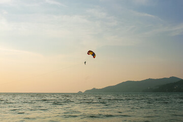 Stunning aerial landscape of Thailand with a colorful parachute gliding over lush tropical scenery, mountains, and turquoise sea.