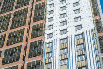Fototapeta premium Construction work on the exterior cladding. Laying waterproofing material on the walls of a high-rise building. Insulation of the house. Balconies of a house under construction.