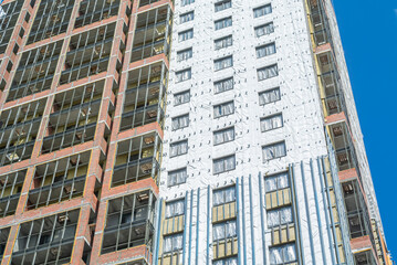 Fototapeta premium Construction work on the exterior cladding. Laying waterproofing material on the walls of a high-rise building. Insulation of the house. Balconies of a house under construction.