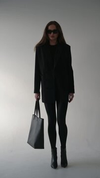 Beautiful young woman in black jacket and sunglasses with bag on white background, style and fashion