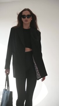 Beautiful young woman in black jacket and sunglasses with bag on white background, style and fashion