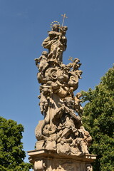 Obraz premium Baroque religious monument with sculpted saints and angels under a clear blue sky. Historic stone statue adorned with Christian symbols in a public space.
