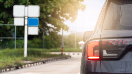 Luxury of grey car with turn on brake light. Side view of concrete road with footpath. On footbath with green grass and trees with bank of siege board trees pieces. With bright light from the front.