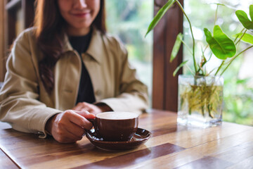Closeup image of a woman holding a cup of hot coffee in cafe