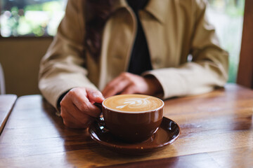 Closeup image of a woman holding a cup of hot coffee with latte art